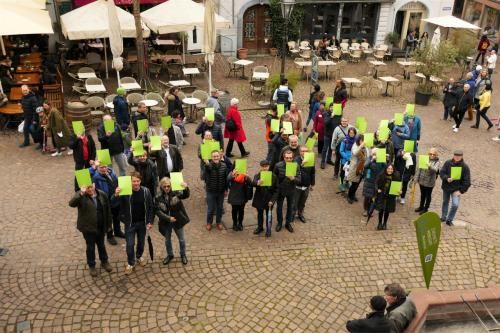 Mitwirkende der Zukunftswerkstatt stehen draußen auf dem Marktplatz und halten grüne Schilder in die Luft, welche zusammen die Buchstaben ZUK bilden.