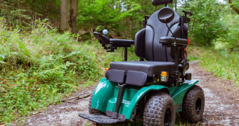 Ein grüner Rollstuhl für das Gelände auf einem Waldweg