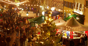 Buden beim Weihnachtsmarkt auf dem Marktplatz, schön beleuchtet mit vielen Besuchern