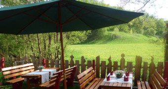 Blick auf grüne Wiesen vom Biergarten mit Sitzgelegenheiten unter einem grünen Sonnenschrim