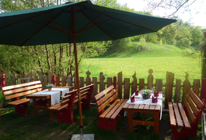 Blick auf grüne Wiesen vom idyllischen Biergarten mit Sitzmöglichkeiten unter einem grüenen Sonennschirm