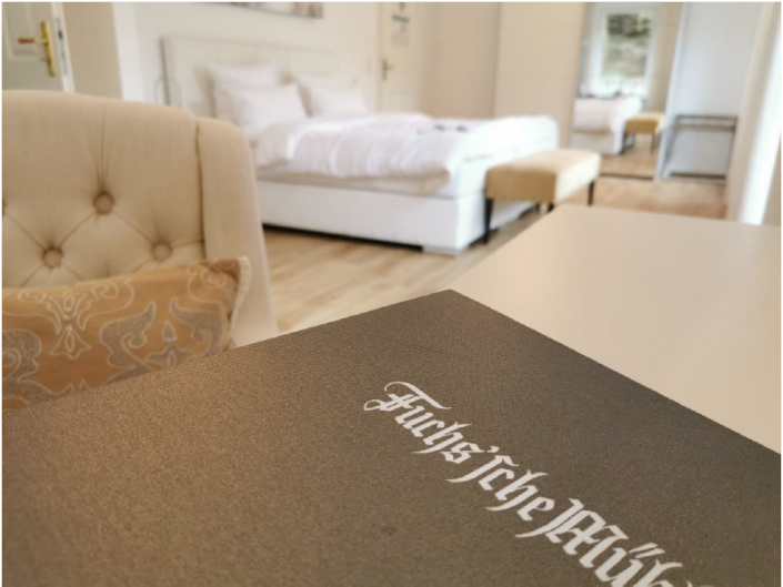 Begrüßungsmappe des Hotels, im Hintergrund ein Zimmer mit Doppelbett
