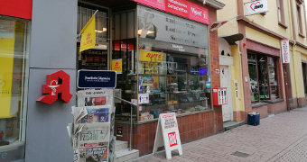 Zeitungsaufsteller vor dem Eingang neben dran ein großes Schaufenster 
