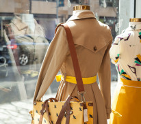 Blick aus einem Schaufenster mit einer Schaufensterpuppe im beigen Mantel mit Umhängetasche.