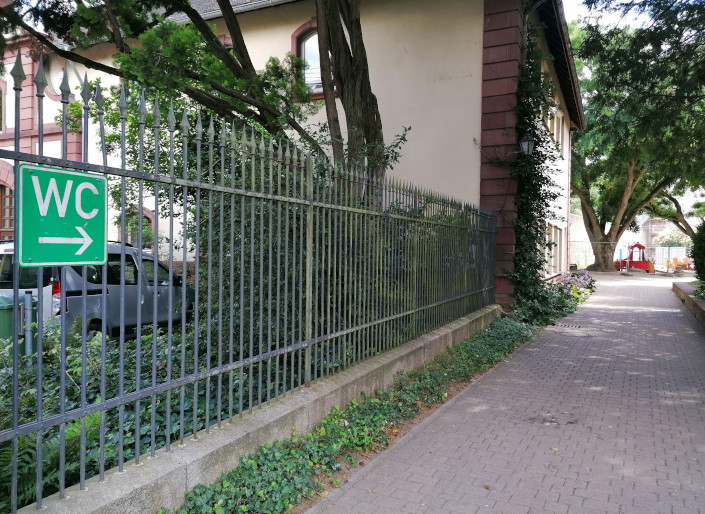 Grünes Schild mit WC und Pfeil in Richtung der öffentlichen Toiletten im Schlosspark