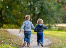 zwei kleine Kinder rennen auf einem Weg in einer Parkanlage Hand in Hand